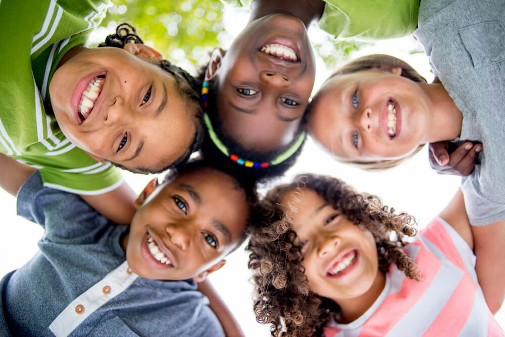 Children in a circle with their arms around each others shoulders smiling down at the camera