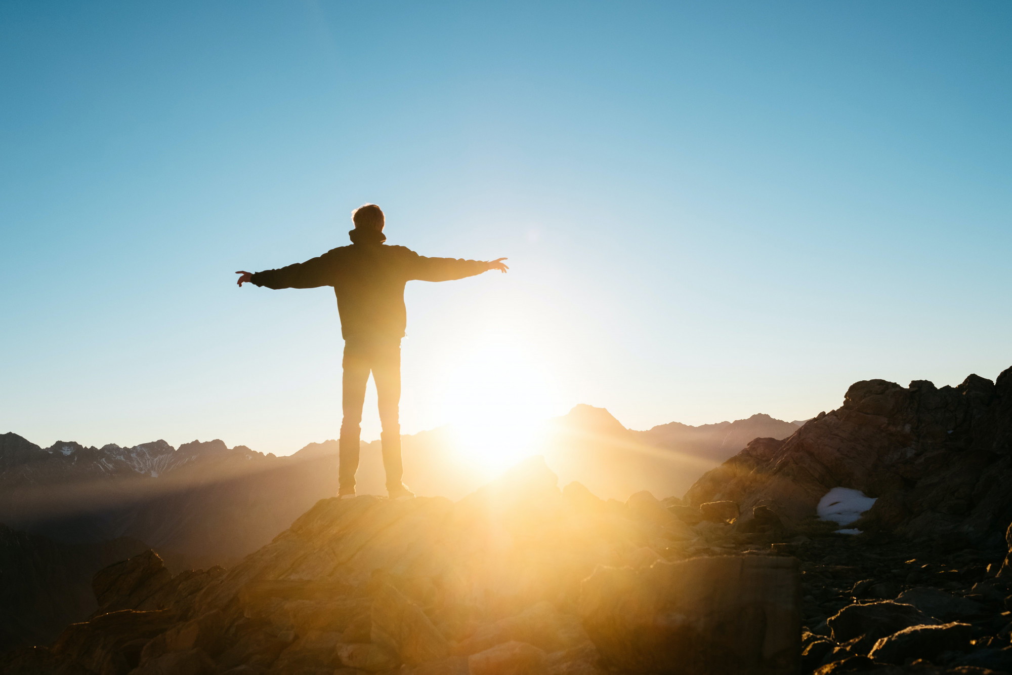 man on mountain looking at sunrise