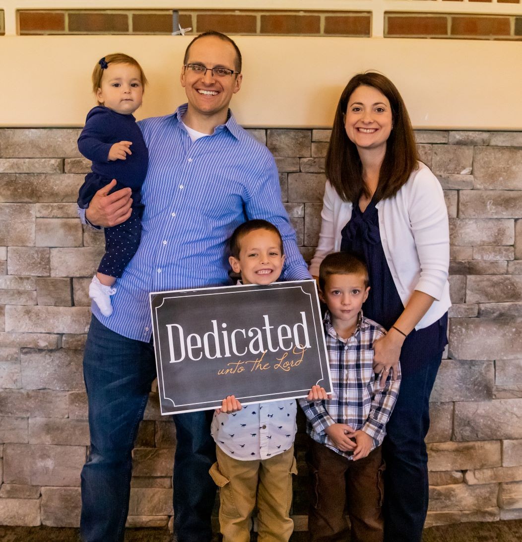Paul and Ashlee's family holding a sign that says "Dedicated unto the Lord"